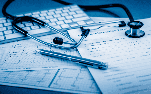 Gros plan bleuté d'un stéthoscope, d'un clavier et d'un stylo sur des formulaires médicaux