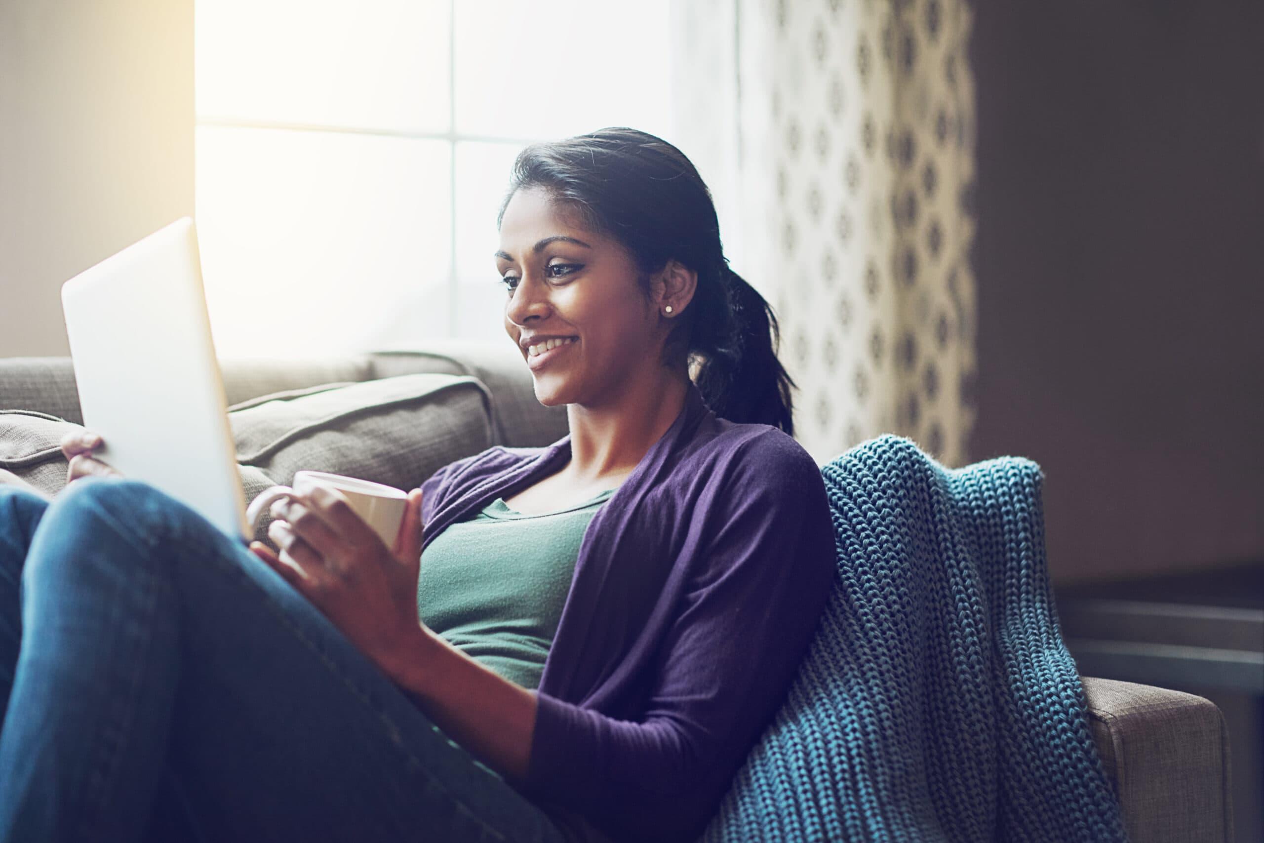 Shot of a young woman using a digital tablet and having coffee on the sofa at home