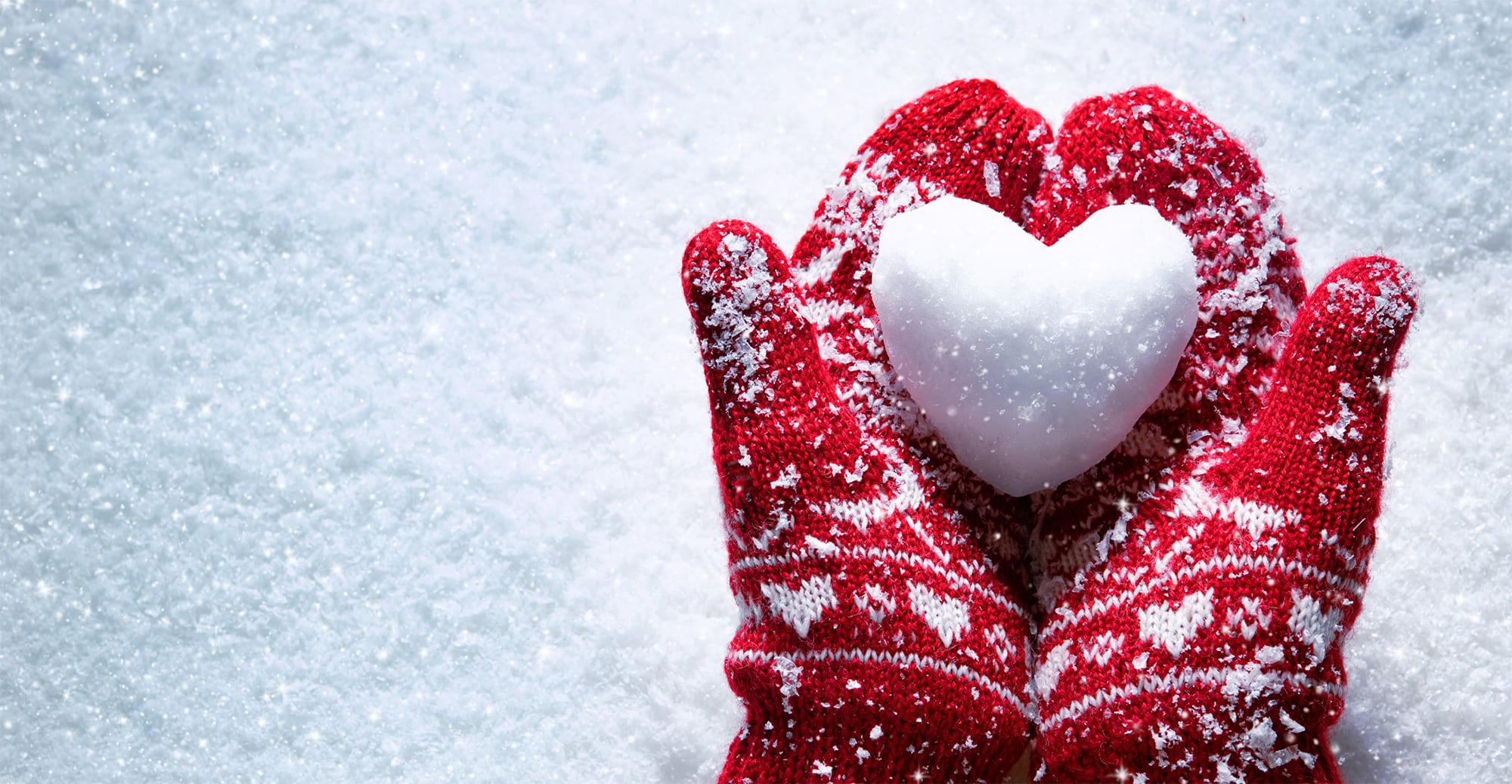 Red mittens holding a snowball shaped as a heart