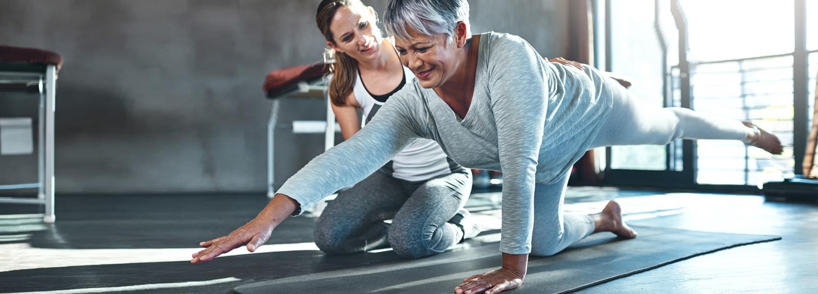 Une entraîneure personnelle aide une femme âgée à s'étirer sur un tapis de yoga