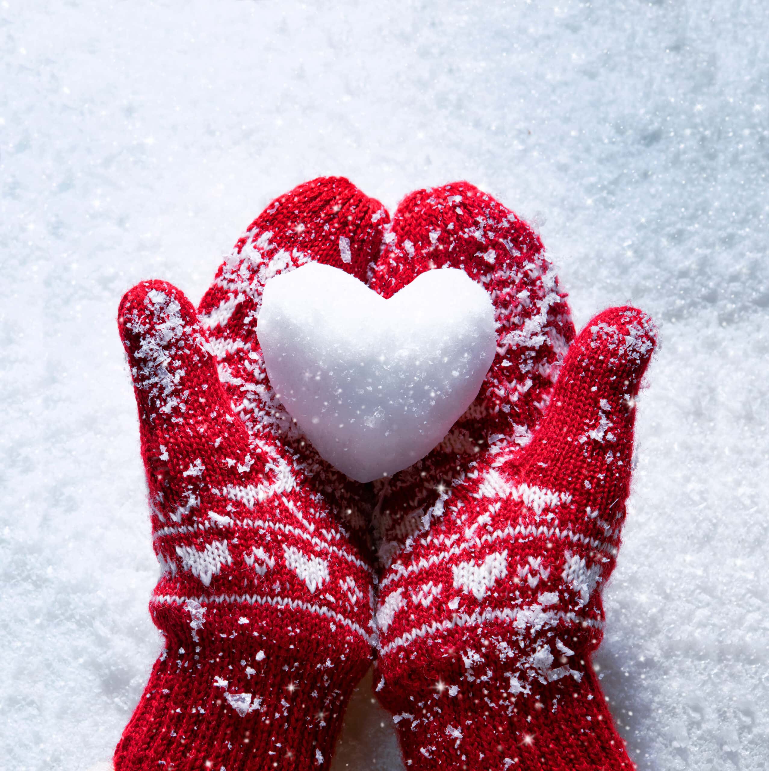 Red mittens holding a snowball shaped as a heart