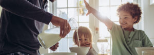Man pouring milk into bowl of cereal with kids